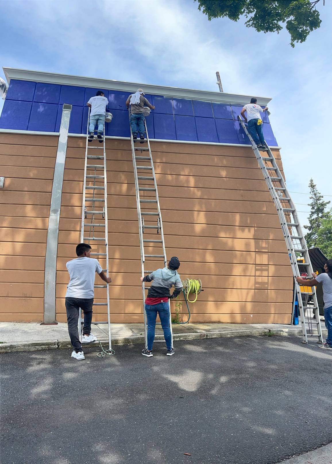 HRF crew applying exterior coating to a commercial building facade using extension ladders